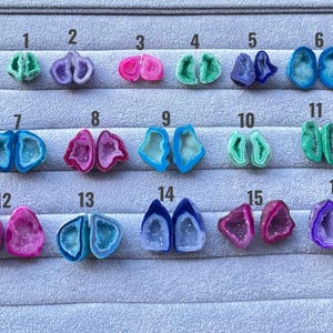 Könnte beinhalten: Sechzehn Paare kleiner, bunter Achat-Geodenscheiben, angeordnet in Reihen auf einem grauen Samt-Präsentiertablett. Jedes Paar ist von 1 bis 16 nummeriert und weist kristalline Zentren in Blau-, Rosa-, Lila-, Grün- und Türkistönen mit polierten Rändern auf.