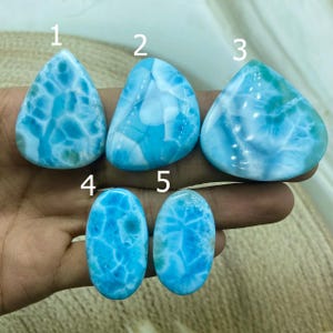 Pu&ograve; includere: Cinque pietre preziose di larimar lucide in varie forme. Le pietre mostrano una gamma di tonalit&agrave; blu con marmorizzazioni bianche, creando un aspetto simile al mare. Le forme includono forme a goccia e ovali, mostrando i modelli naturali.