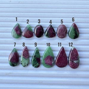 May include: Twelve polished ruby zoisite gemstones arranged in two rows of six, each numbered from 1 to 12. The stones feature varying patterns of deep magenta-red ruby inclusions set within a vibrant green zoisite matrix, with teardrop and oval shapes.