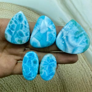 Pu&ograve; includere: Una collezione di sei pietre preziose di larimar lucidate. Le pietre variano nella forma, tra cui forme a goccia e ovali. Il larimar presenta un sorprendente motivo blu e bianco, con alcune pietre che mostrano sfumature di verde.