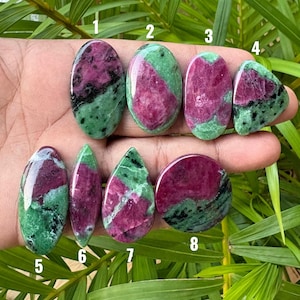 Puede incluir: Ocho cabujones de rubí en zoisita pulidos de diversas formas, incluyendo ovalada, gota y redonda, cada uno con una mezcla distintiva de inclusiones de rubí magenta-rosa intenso en una matriz de zoisita verde vibrante con motas negras.
