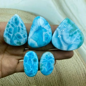 Pu&ograve; includere: Una collezione di sei pietre preziose di larimar lucidate in varie forme. Le pietre presentano un vibrante colore blu con venature bianche, che ricordano le onde dell'oceano. Le forme includono gocce, triangoli e ovali, mettendo in risalto la bellezza naturale del minerale.