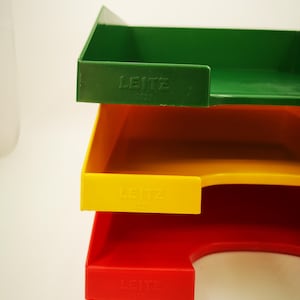 Könnte beinhalten: Ein Stapel von drei farbigen Leitz-Briefablagen in Grün, Gelb und Rot. Jede Ablage hat den Markennamen Leitz und die Nummer 5227 auf der Vorderseite eingeprägt. Die Ablagen sind aus Kunststoff und dienen zum Ordnen von Dokumenten.