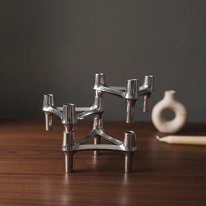 Peut inclure: Un bougeoir modulaire en métal argenté présentant un design géométrique imbriqué avec plusieurs supports cylindriques pour bougies. La structure est composée de plusieurs segments connectés créant un aspect étagé à plusieurs niveaux.