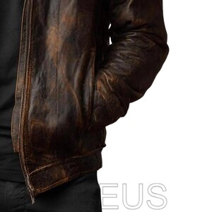 May include: A brown leather jacket with a distressed, vintage appearance. The jacket has a zip closure and pockets. The leather has a worn, textured look with colour variations, suggesting age and use. A classic outerwear piece.