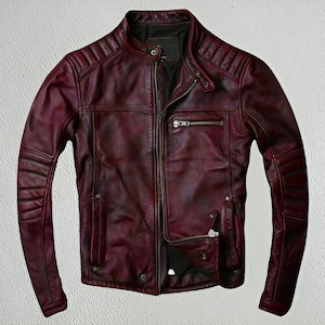 May include: A burgundy leather jacket with a stand-up collar and a zip-up front. The jacket has quilted detailing on the shoulders and sleeves, with multiple zippered pockets. The jacket is a deep red color.