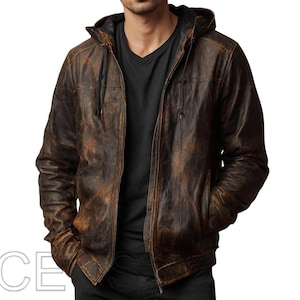 Puede incluir: Chaqueta de cuero marrón con acabado envejecido, con capucha y cremallera. La chaqueta tiene dos bolsillos delanteros y un forro negro. La chaqueta se lleva sobre una camiseta negra con cuello en V.