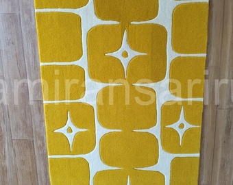 Può includere: Un tappeto rettangolare con un design retrò. Il tappeto presenta un motivo di quadrati gialli e forme a stella su sfondo bianco. Il tappeto è realizzato in un materiale morbido e strutturato ed è posizionato su un pavimento in legno.