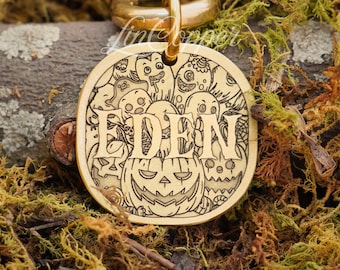 May include: A round gold-toned metal pet tag featuring an engraved pattern of various cartoon monsters, ghosts, and a jack-o'-lantern. The name EDEN is prominently engraved in large capital letters across the center of the circular tag.