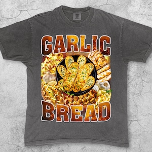 May include: Dark gray t-shirt with a graphic of garlic bread. The graphic features a plate of garlic bread, garlic cloves, and the words "GARLIC BREAD" in a brown, textured font. The word "Pepper" is printed at the bottom left.
