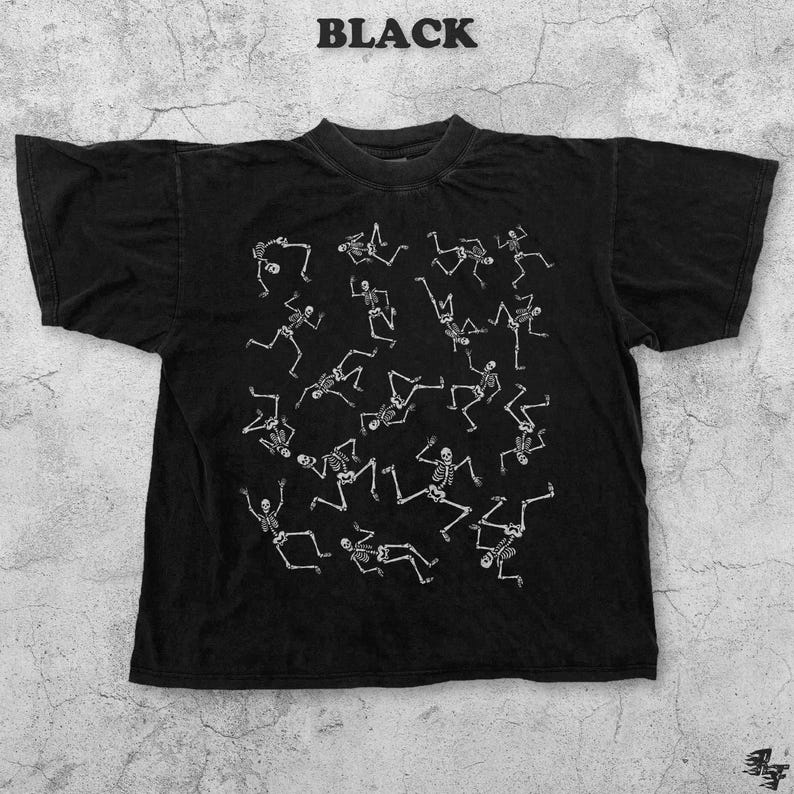 May include: Black t-shirt with a crew neck and short sleeves. The shirt features a white graphic of multiple skeletons in various poses. The word "BLACK" is printed in white at the top of the shirt.