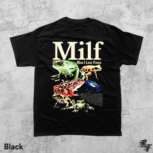 May include: Black t-shirt with the text "MILF: Man I Love Frogs" in a bold, cream-colored font. The shirt features a colorful graphic of various frog species. The word "Black" is printed at the bottom left.