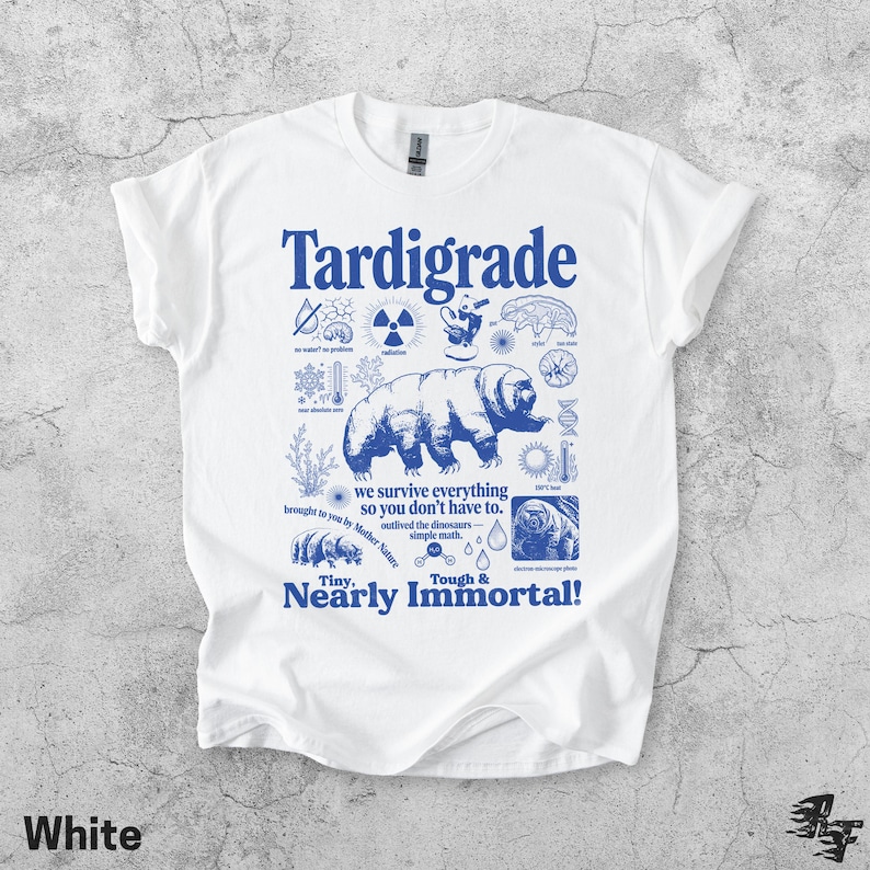 Puede incluir: Una camiseta blanca de manga corta con un estampado gr&aacute;fico azul de un tard&iacute;grado rodeado de iconos cient&iacute;ficos y textos que incluyen "Tardigrade", "we survive everything so you don't have to" y "Tiny, Nearly Immortal!" en estilo vintage.