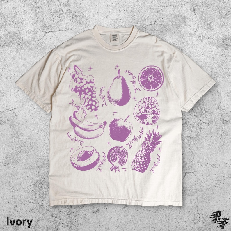 Pu&ograve; includere: T-shirt color avorio con illustrazione di frutta viola. Il design include uva, una pera, una fetta d'arancia, banane, una mela, un lampone, una pesca, un melograno e un ananas. La parola "Ivory" &egrave; stampata in basso.
