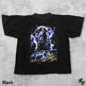 Puede incluir: Camiseta negra con un gr&aacute;fico de un lobo aullando sobre un fondo de tormenta el&eacute;ctrica. El dise&ntilde;o incluye varios lobos en un entorno forestal. La palabra "Black" est&aacute; impresa en la parte inferior de la camiseta.