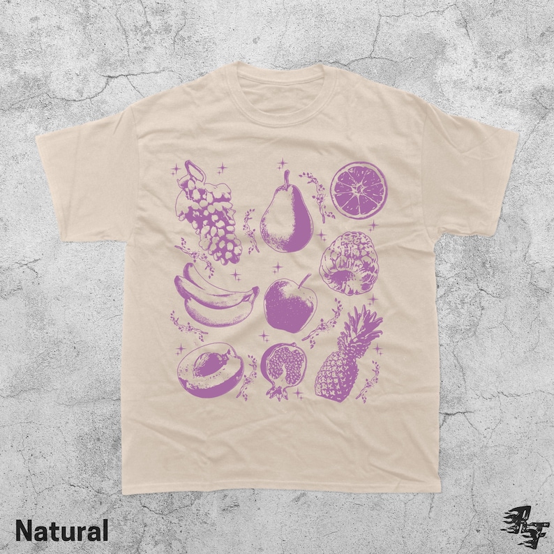 Pu&ograve; includere: T-shirt beige con illustrazione di frutta viola. Il design include uva, una pera, un'arancia a fette, una banana, una mela, una prugna, un melograno e un ananas. La parola "Natural" &egrave; stampata in basso.