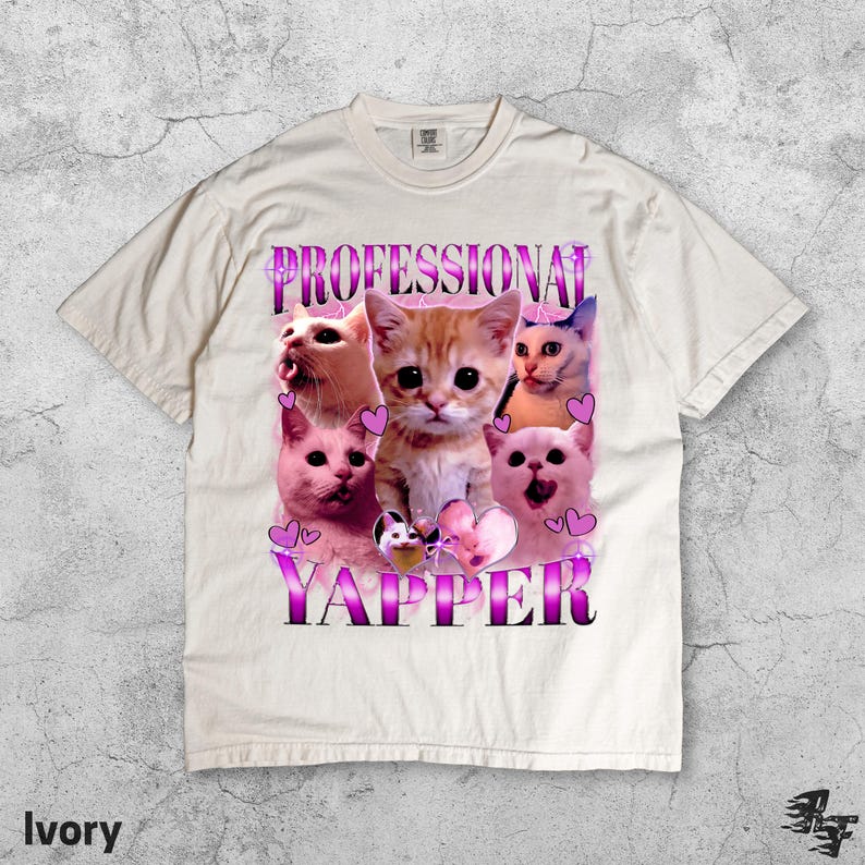 May include: Ivory-colored t-shirt featuring a graphic of several cats with the text "PROFESSIONAL YAPPER" in a purple and white font. The cats have various expressions, and pink hearts are scattered around the design.