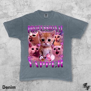 May include: Denim blue t-shirt featuring a graphic of several cats with the text "PROFESSIONAL YAPPER" in a pink and purple font. The cats are in various poses, with hearts around them.