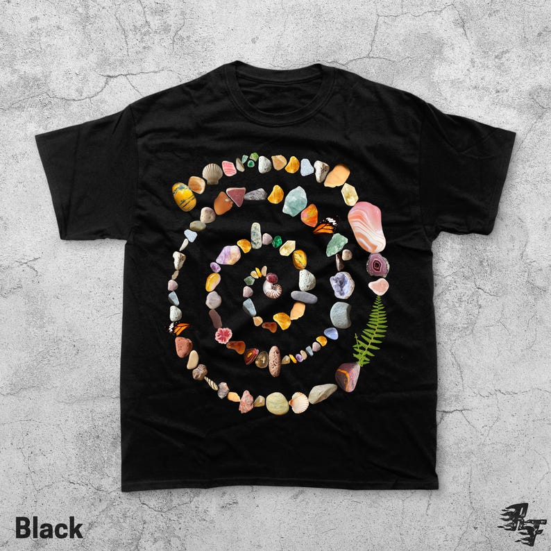 Puede incluir: Camiseta negra con un dise&ntilde;o en espiral hecho de varias piedras de colores, conchas y un helecho. La palabra "Black" est&aacute; impresa en la esquina inferior izquierda de la camiseta.