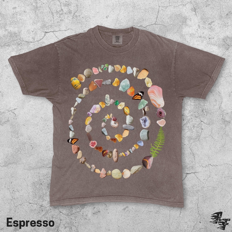 Puede incluir: Camiseta color espresso con un dise&ntilde;o en espiral hecho de piedras, conchas e ilustraciones de mariposas. La camiseta tiene cuello redondo y mangas cortas. La palabra "Espresso" est&aacute; impresa en la parte inferior.