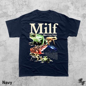 May include: Navy blue t-shirt featuring the word "Milf" above the phrase "Man I Love Frogs" and a collage of colorful frog illustrations. The shirt includes a detailed description of frogs.