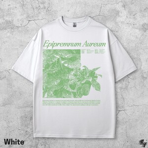 May include: White t-shirt featuring a green botanical illustration of Epipremnum Aureum, with the plant's name in a stylized font. The shirt also includes a description of the plant. The word "White" is printed at the bottom.