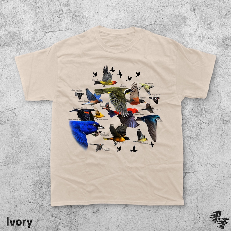 May include: Ivory-colored t-shirt featuring a colorful illustration of various bird species, each labeled with their name. The design includes birds in flight and perched, with a variety of colors and patterns. The word "Ivory" is printed at the bottom.