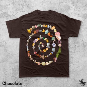 Puede incluir: Camiseta marr&oacute;n chocolate con un dise&ntilde;o en espiral hecho de piedras, conchas y un helecho. La palabra "Chocolate" est&aacute; impresa en la parte inferior. El dise&ntilde;o es una colecci&oacute;n de elementos naturales.