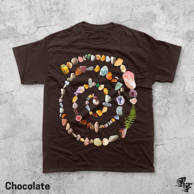 Puede incluir: Camiseta marr&oacute;n chocolate con un dise&ntilde;o en espiral hecho de piedras, conchas y un helecho. La palabra "Chocolate" est&aacute; impresa en la parte inferior. El dise&ntilde;o es una colecci&oacute;n de elementos naturales.