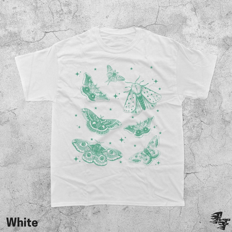 May include: White t-shirt featuring a collection of green moth illustrations and stars. The moths vary in size and design, with intricate wing patterns. The word "White" is printed at the bottom left corner of the shirt.