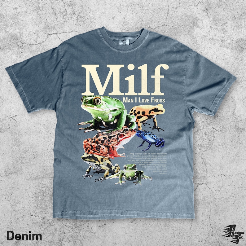 May include: Denim blue t-shirt with the word "Milf" in large white letters above a collection of colorful frog illustrations. The phrase "Man I Love Frogs" is printed below the word "Milf".