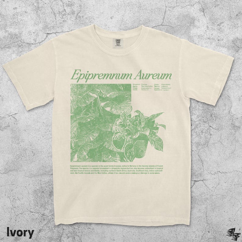 May include: Ivory-colored t-shirt with a green botanical illustration and the text "Epipremnum Aureum." The design features a detailed drawing of a plant with leaves and stems. The shirt also includes additional text describing the plant's origin.