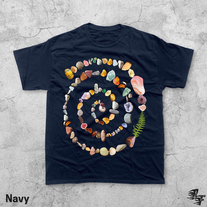Puede incluir: Camiseta azul marino con un dise&ntilde;o en espiral hecho de varias piedras, conchas y un helecho coloridos. La palabra "Navy" est&aacute; impresa en la esquina inferior izquierda.