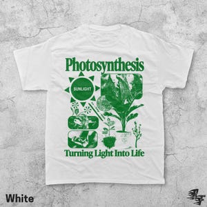Op de afbeelding: Wit T-shirt met een groen grafisch ontwerp met het woord "Photosynthese" en illustraties van planten, een zon en de tekst "Turning Light Into Life". Het shirt heeft een ronde hals en korte mouwen.