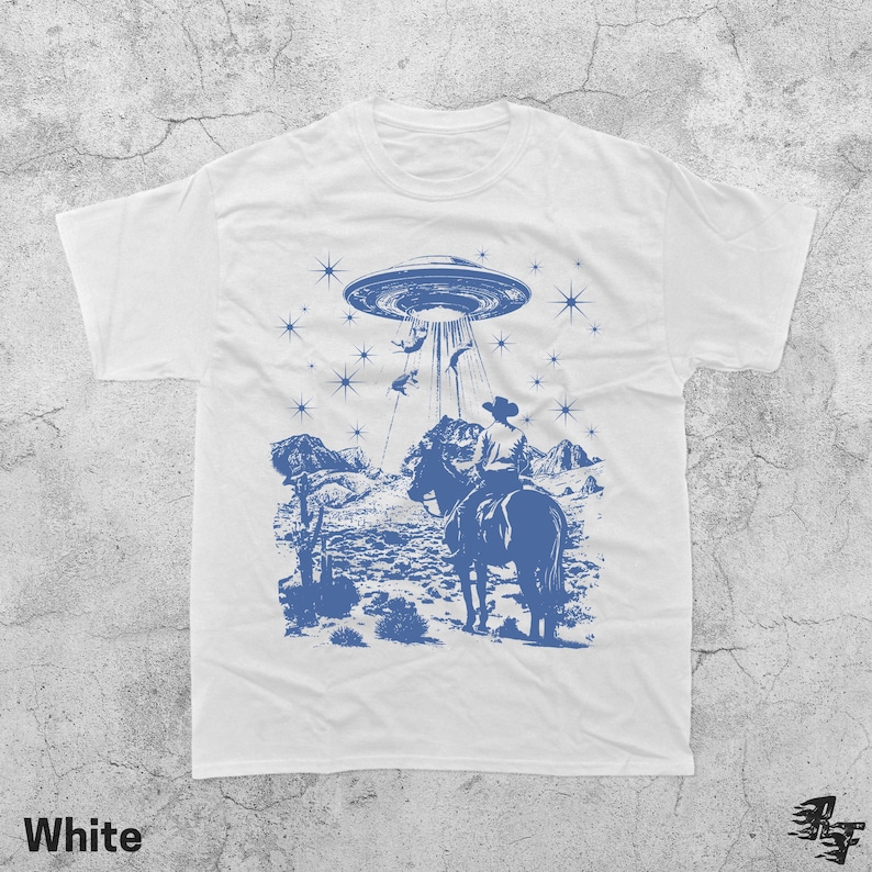 May include: White t-shirt with a blue graphic of a cowboy on horseback being abducted by a UFO. The design includes a desert landscape, stars, and the word "White" at the bottom.