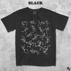May include: Black t-shirt with a white skeleton pattern. The word "BLACK" is printed at the top. The design features multiple white skeletons in various poses, creating a playful and spooky aesthetic.