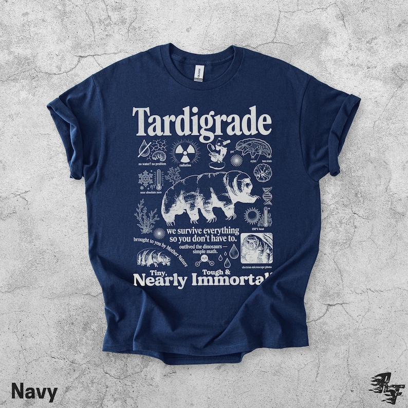 Puede incluir: Una camiseta azul marino con un estampado gr&aacute;fico blanco de un tard&iacute;grado rodeado de iconos cient&iacute;ficos y textos que incluyen "Tardigrade", "we survive everything so you don't have to", "Tiny, Tough & Nearly Immortal" y "outlived the dinosaurs".