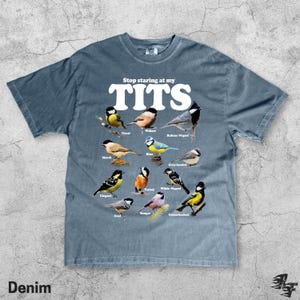 May include: Denim blue t-shirt with the text "Stop staring at my TITS" in white. The shirt features illustrations of various bird species, including Great, Willow, and Rufous-Naped birds. The word "Denim" is printed at the bottom.