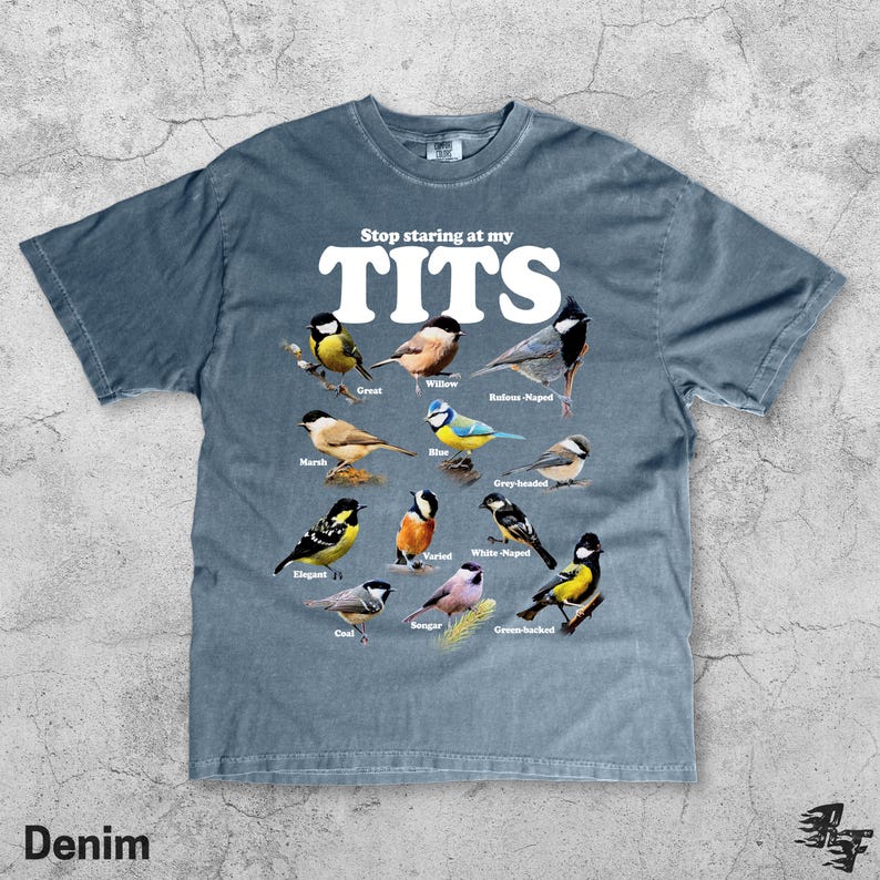 May include: Denim blue t-shirt with the text "Stop staring at my TITS" in white. The shirt features illustrations of various bird species, including Great, Willow, and Rufous-Naped birds. The word "Denim" is printed at the bottom.