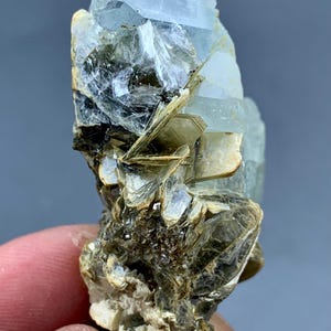 Peut inclure: Un amas de cristaux d'aigue-marine bruts, de couleur bleu p&acirc;le. Le cristal a une structure en couches avec une surface rugueuse et textur&eacute;e. La base de l'amas est un m&eacute;lange de min&eacute;raux bruns et beiges, cr&eacute;ant un aspect naturel et terreux.