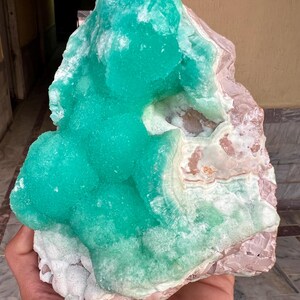 May include: A large, raw mineral specimen featuring a vibrant, crystalline turquoise formation atop a matrix of pink and white stone. The mineral's surface has a textured, bubbly appearance, contrasting with the smoother base. The overall shape is irregular and natural.