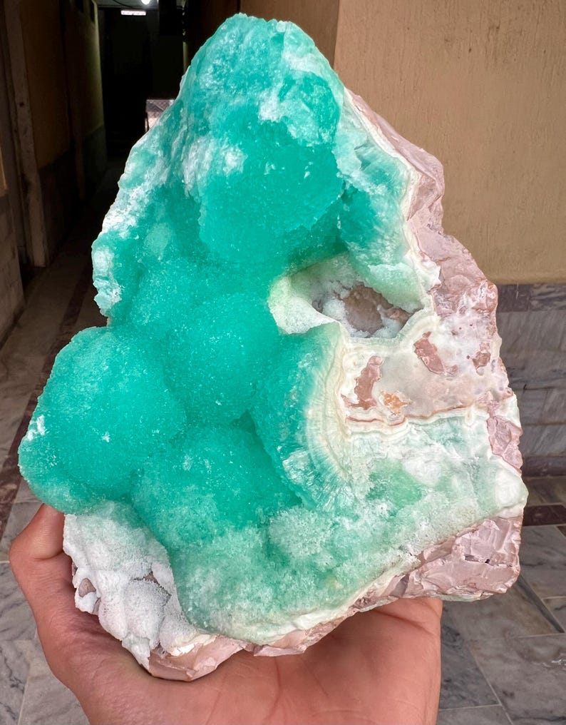 May include: A large, raw mineral specimen featuring a vibrant, crystalline turquoise formation atop a matrix of pink and white stone. The mineral's surface has a textured, bubbly appearance, contrasting with the smoother base. The overall shape is irregular and natural.