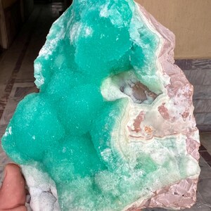May include: A large, raw mineral specimen featuring a vibrant, crystalline turquoise formation atop a base of pink and white stone. The rough-hewn edges and natural textures are visible, showcasing the stone's unique geological composition.
