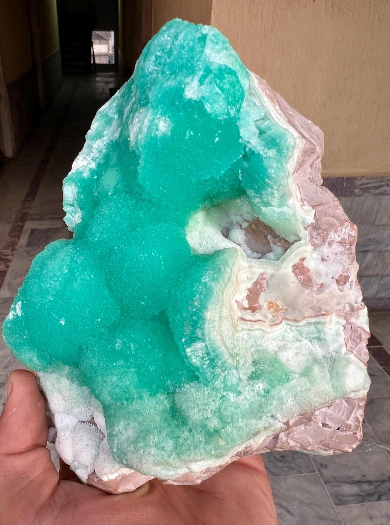 May include: A large, raw mineral specimen featuring a vibrant, crystalline turquoise formation atop a base of pink and white stone. The rough-hewn edges and natural textures are visible, showcasing the stone's unique geological composition.