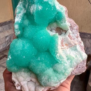 May include: A vibrant, natural mineral specimen featuring a striking combination of colors and textures. The focal point is a cluster of bright turquoise-green crystals, contrasted against a base of pink and white rock. The overall form is organic and irregular.