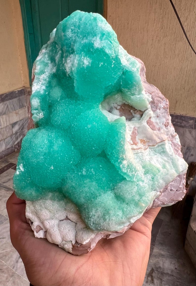 May include: A vibrant, natural mineral specimen featuring a striking combination of colors and textures. The focal point is a cluster of bright turquoise-green crystals, contrasted against a base of pink and white rock. The overall form is organic and irregular.