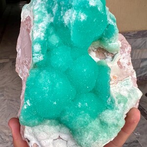 May include: A large, raw mineral specimen featuring a vibrant, crystalline turquoise formation atop a matrix of pink and white stone. The rough texture and natural colors create a striking display.