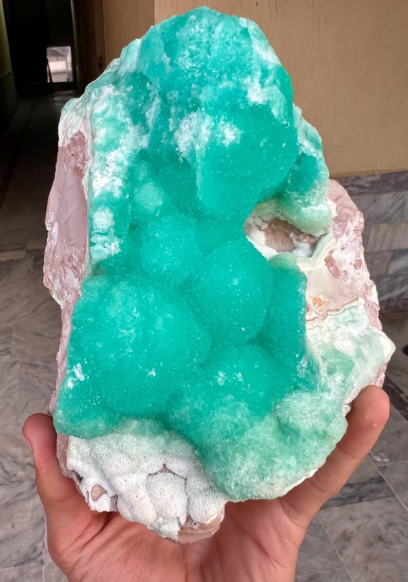 May include: A large, raw mineral specimen featuring a vibrant, crystalline turquoise formation atop a matrix of pink and white stone. The rough texture and natural colors create a striking display.