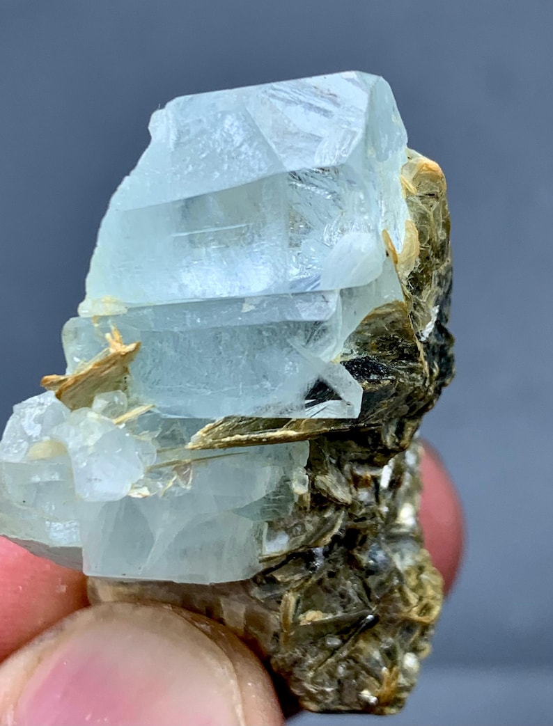 Peut inclure: Un amas de cristaux d'aigue-marine bleu clair avec une texture naturelle rugueuse. Le cristal a une qualit&eacute; translucide, avec des structures internes visibles. La base de l'amas est un m&eacute;lange de min&eacute;raux bruns et noirs.