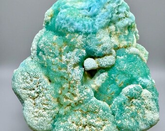 Op de afbeelding: Een levendig, natuurlijk mineraal specimen met een getextureerd oppervlak. Het mineraal heeft een mix van lichtblauwe en groene tinten, met witte en bruine plekken. De algemene vorm is onregelmatig en organisch, wat de ruwe schoonheid van de steen laat zien.